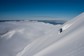 A skier headed down a mountain above the clouds on a clear day.